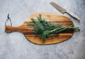 Chopping boar with dill and a knife.